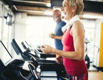 Mature people running in machine treadmill at fitness gym club senior woman smiles while walking on the treadmill at her senior fitness center
