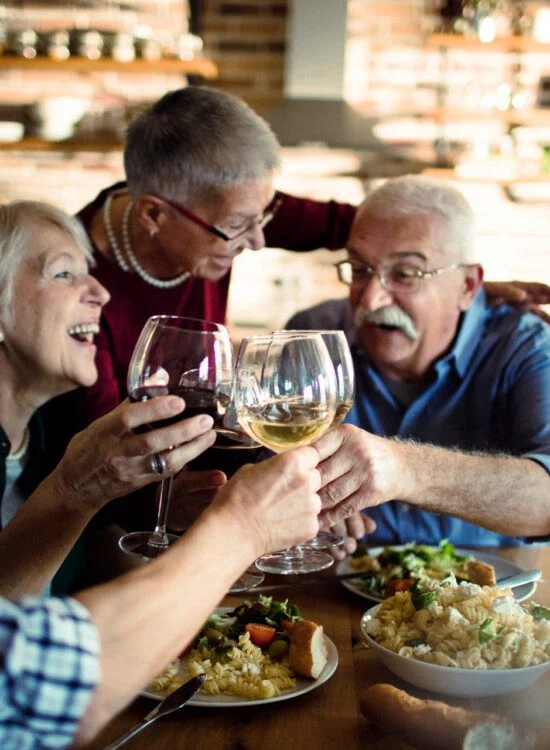 Four people share a meal and toast with wine glasses at a table indoors.