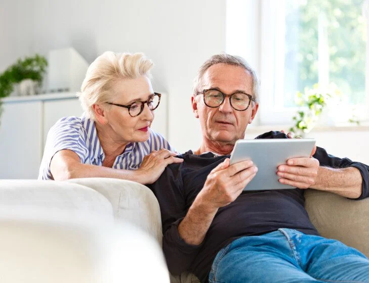 senior couple relaxing at home while looking at a tablet in the senior man's hands