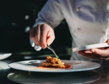 A chef is finishing the preparation of the plate. He's decorating the plate just before the serving. close-up of chef carefully plating elegant meal