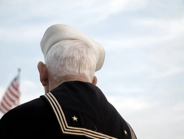 Senior Navy Veteran gazes off into the distance at the American flag