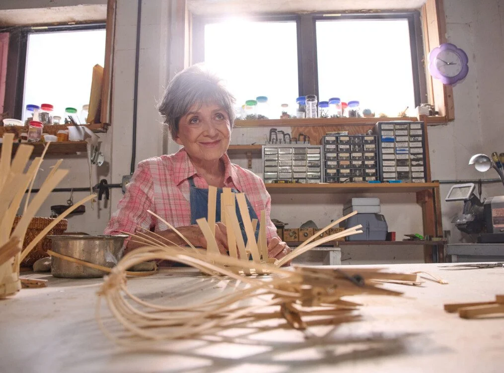 senior woman smiles and looks at an off-camera instructor during a basket-weaving class
