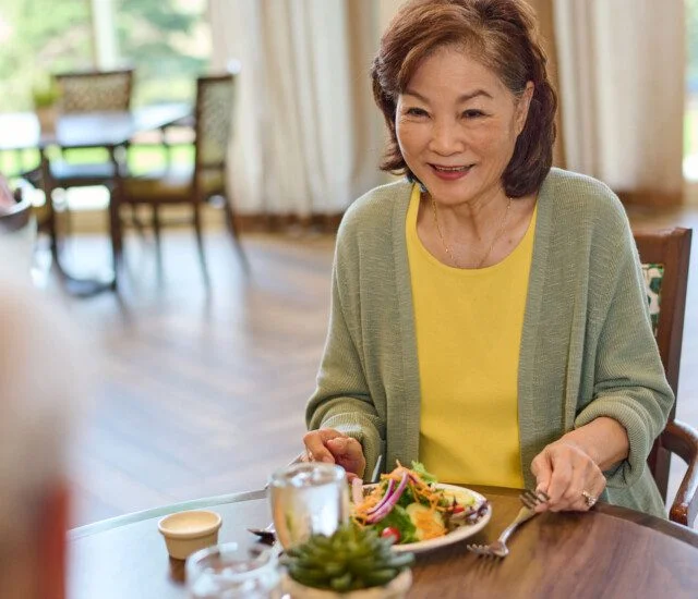 senior woman smiles at her companion while enjoying a healthy lunch in their senior dining room