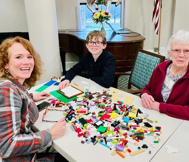 Three people building with colorful LEGO bricks at a table indoors.
