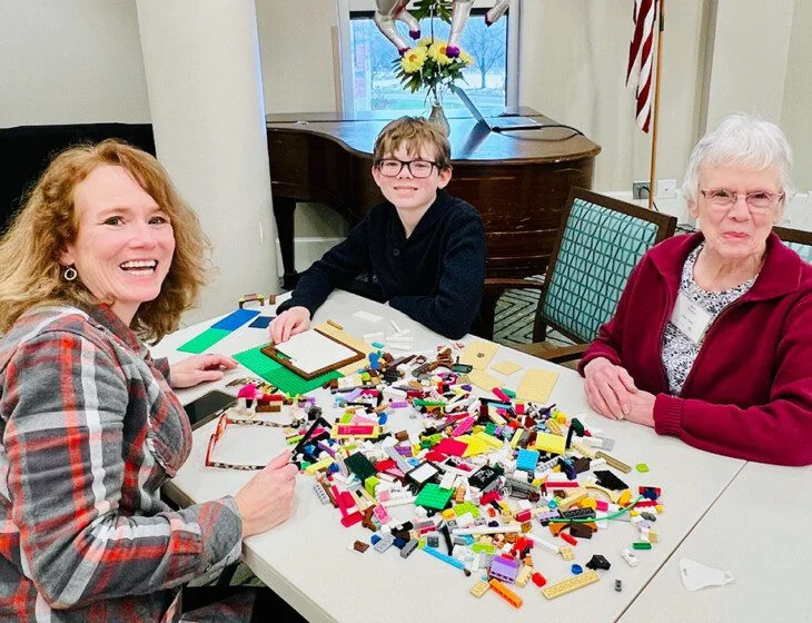 Three people building with colorful LEGO bricks at a table indoors.