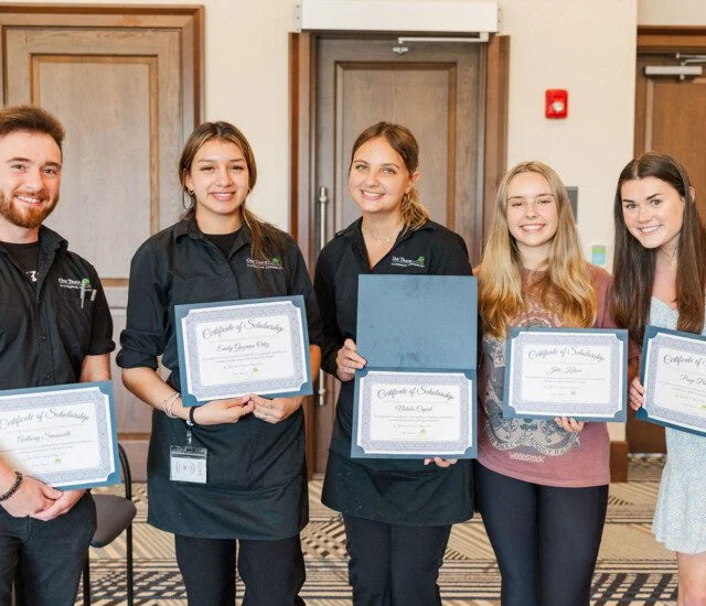 Five people holding certificates and smiling at a ceremony.