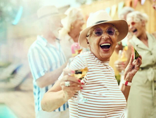 Carefree mature woman having fun with her friends during a summer party by the pool in the backyard and looking at camera.