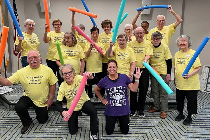 Group of seniors posing with pool noodles in a workout class.