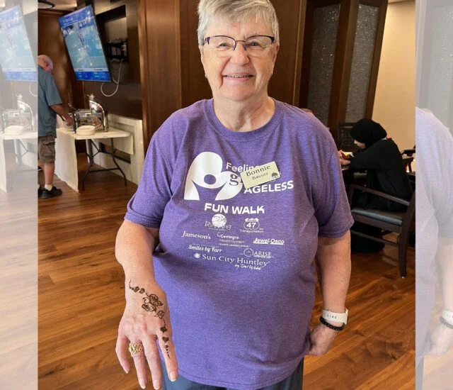 Smiling person in a purple Fun Walk shirt with a henna design on their hand.