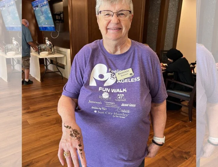 Smiling person in a purple Fun Walk shirt with a henna design on their hand.