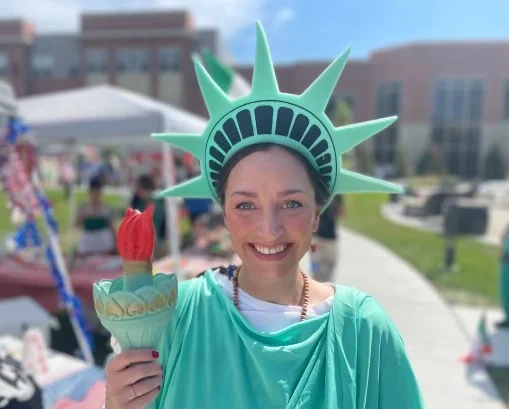 Person dressed as Statue of Liberty, standing outdoors at an event.