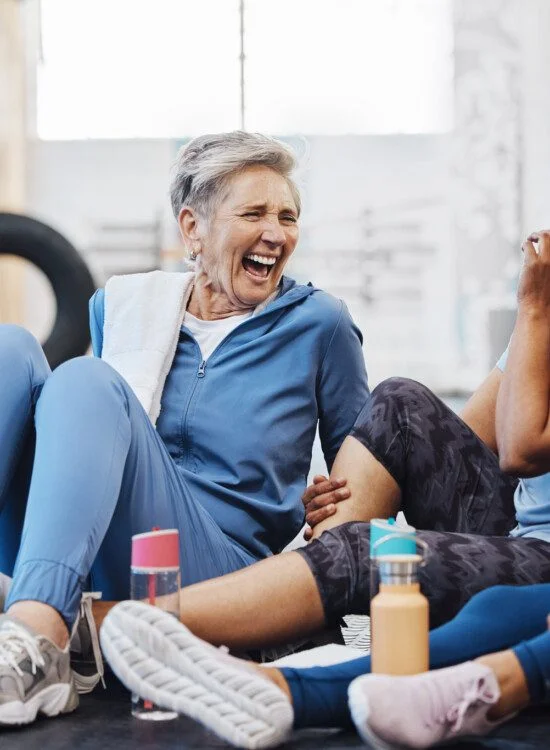 Gym, laughing and group of mature women telling joke after fitness class, conversation and comedy on floor. Exercise, bonding and happy senior woman with friends sitting chatting together at workout.