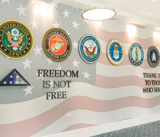 Military branch emblems on a wall with Freedom is not free and Thank you to those who served.