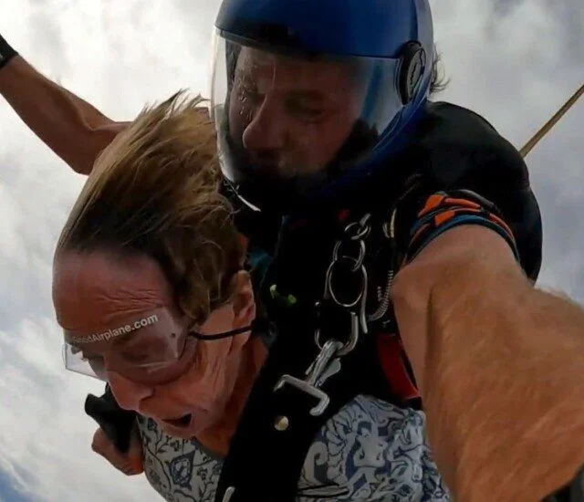 Two people tandem skydiving with a cloudy sky background.