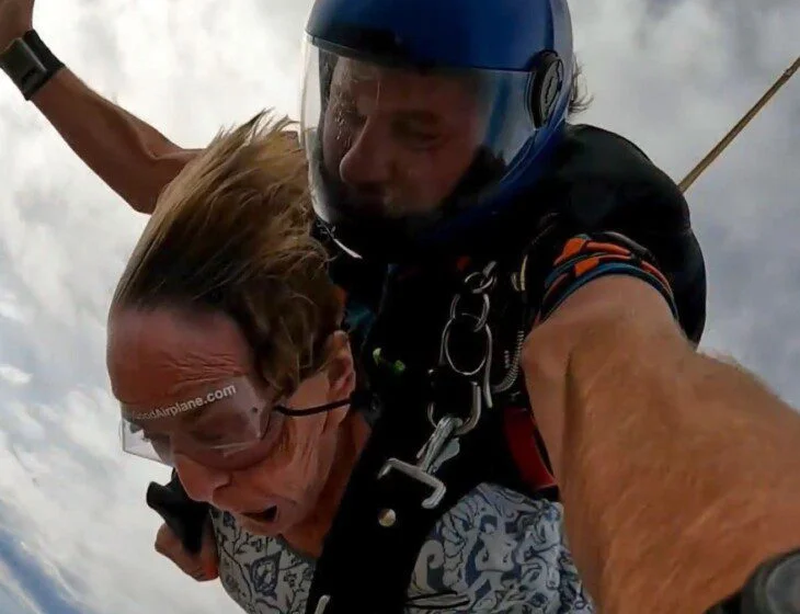 Two people tandem skydiving with a cloudy sky background.