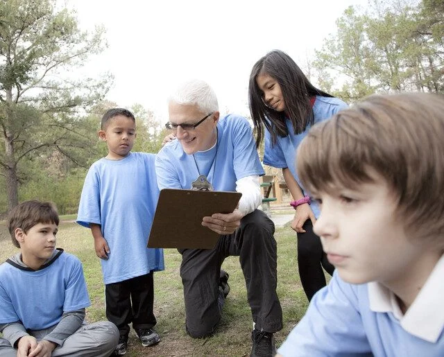 Children and a coach gather outdoors, focusing on a clipboard.