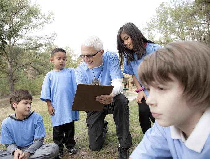 Children and a coach gather outdoors, focusing on a clipboard.