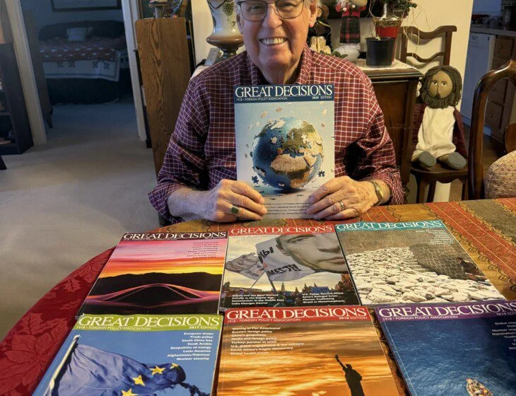 Person holding Great Decisions magazine, surrounded by various editions on a table.