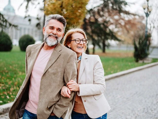 Smiling couple walking arm in arm on a cobblestone path in a park.