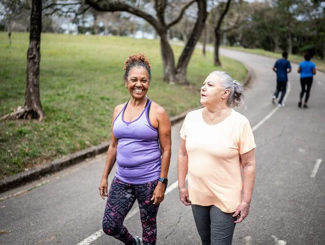 Two women walking on a park path, enjoying an outdoor exercise session.