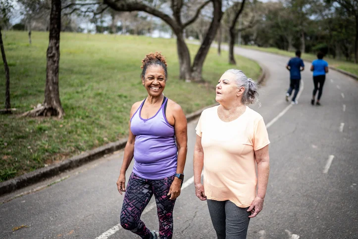 Two women walking on a park path, enjoying an outdoor exercise session.
