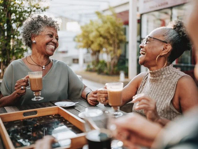 Two women enjoying coffee and laughing together outside at a table.