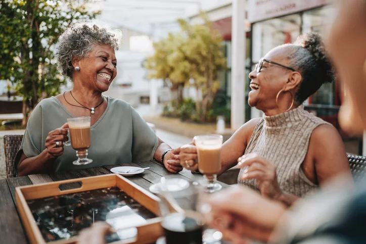 Two women enjoying coffee and laughing together outside at a table.
