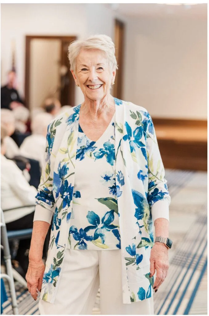 Smiling woman wearing floral outfit in a room, standing with hands by her sides.
