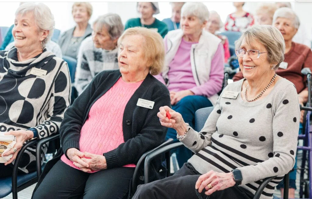 Senior women seated, smiling and attending a group event.