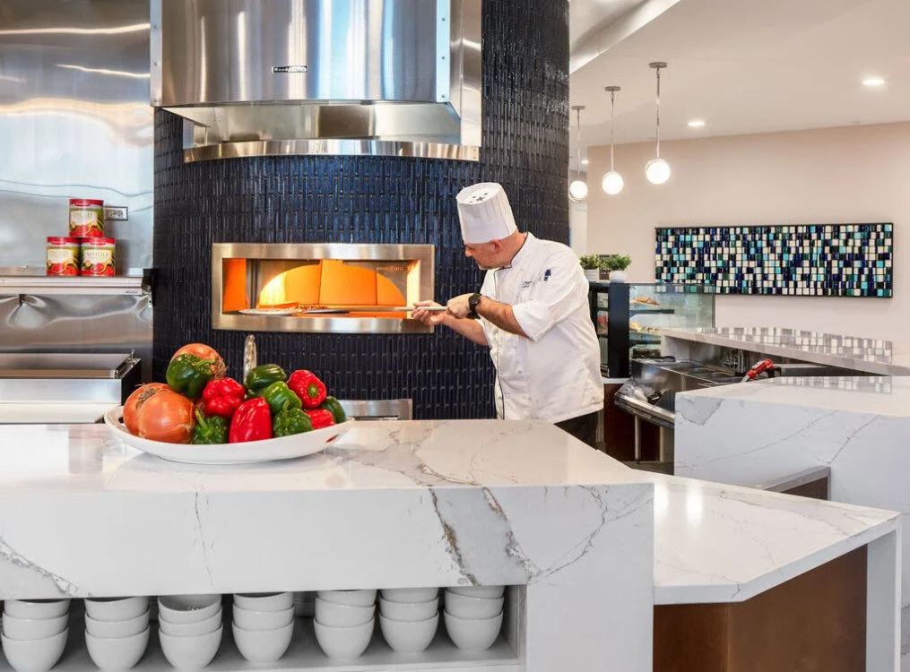 Chef putting food in a brick oven in a modern kitchen.