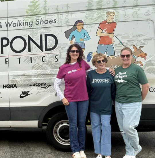 Three people smiling in front of a van with Dick Pond Athletics logo.