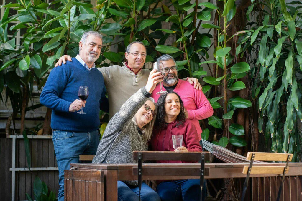 Group of friends toasting with drinks at a patio, surrounded by greenery.
