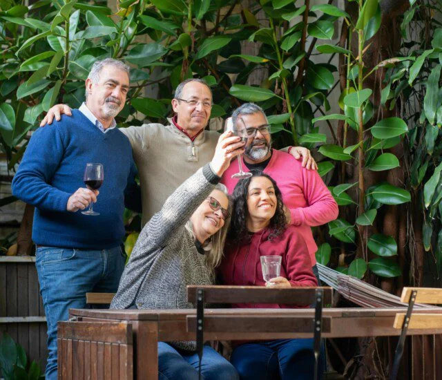 Group of friends toasting with drinks at a patio, surrounded by greenery.