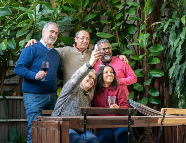 Group of friends toasting with drinks at a patio, surrounded by greenery.