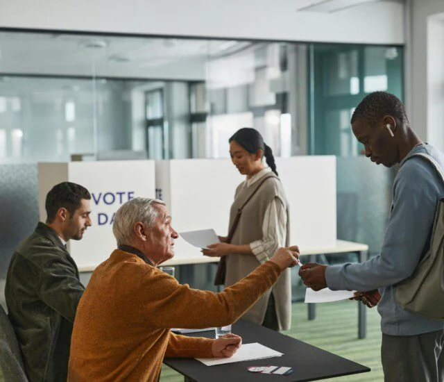 People voting at a polling station with two officials sitting at a table.