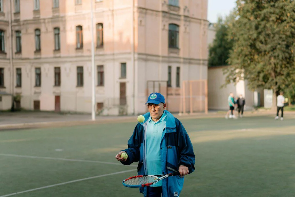 Person juggling tennis balls on a court near a building.