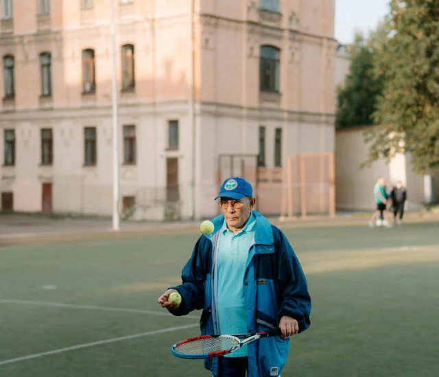 Person juggling tennis balls on a court near a building.