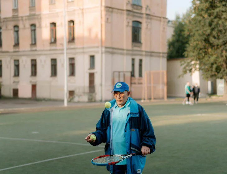 Person juggling tennis balls on a court near a building.