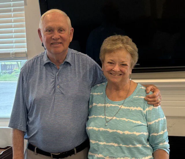 Older couple smiling and standing together indoors.