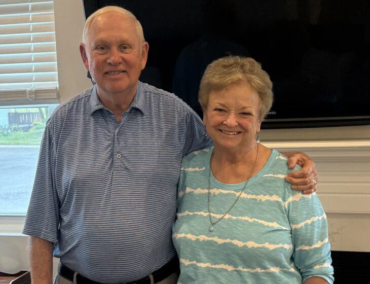 Older couple smiling and standing together indoors.