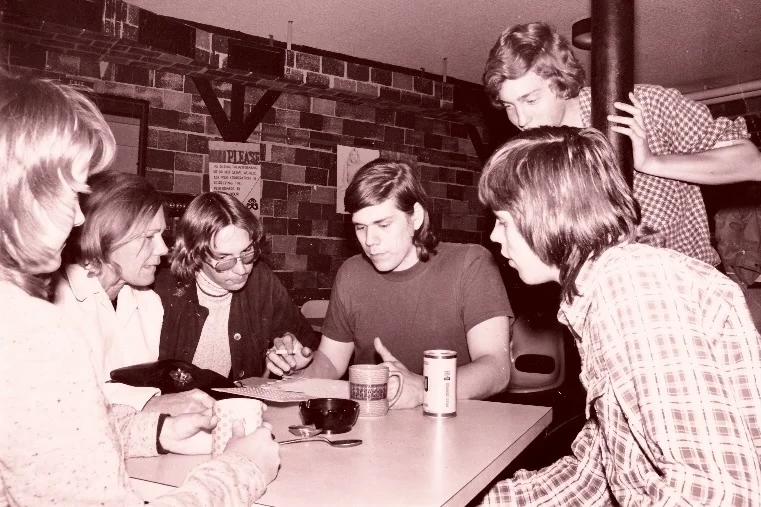 Black and white photo of six people gathered around a table, engaged in discussion.