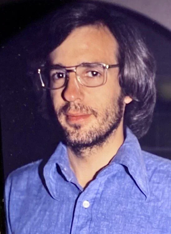 Man with glasses and beard wearing a blue shirt.