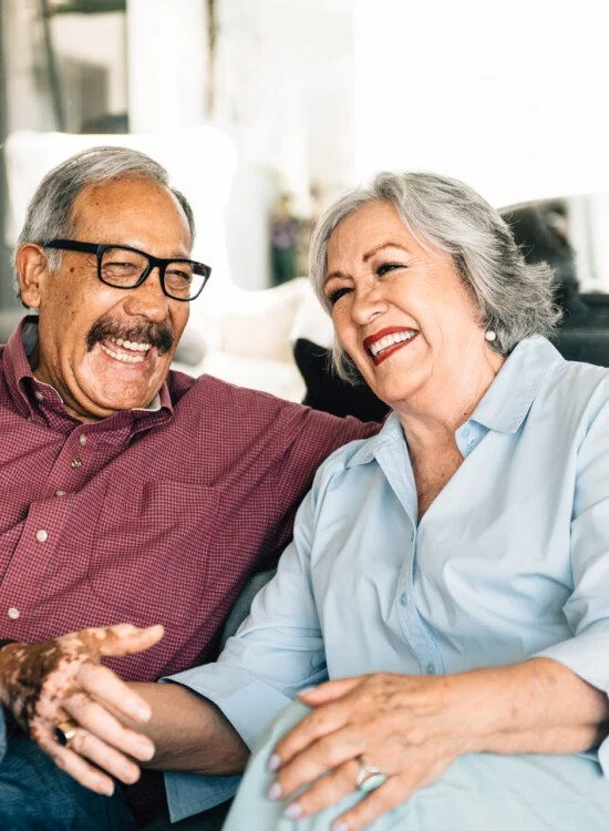 Elderly couple laughing together on a sofa at home.