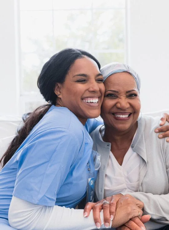Nurse and elderly woman hugging and smiling in a bright room.