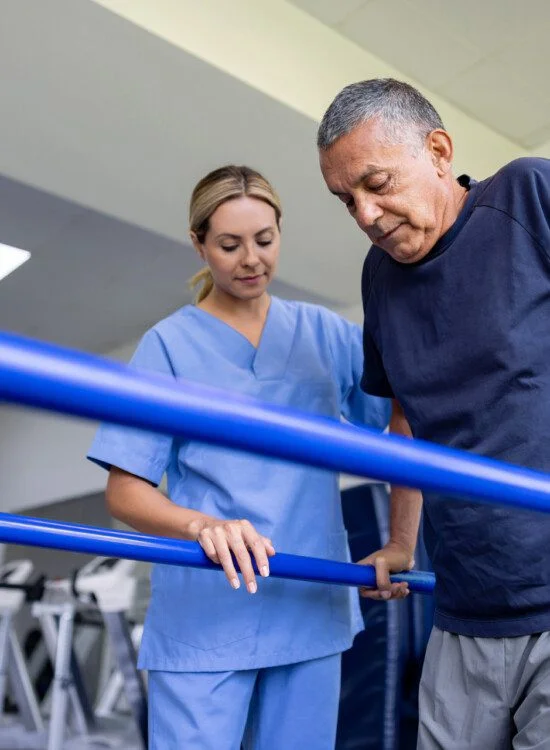 Healthcare worker assists man with physical therapy using parallel bars.