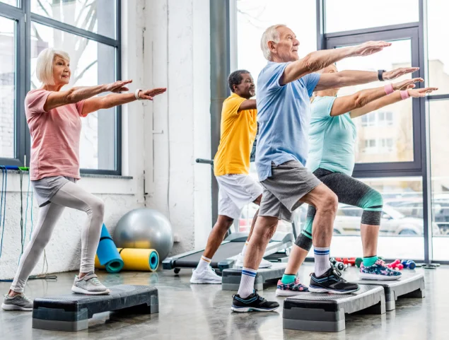 Seniors doing step exercises in fitness class, bright gym setting.