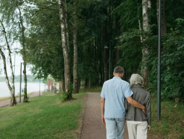 Man with arm around woman's waist walking down a wooded path next to a lake
