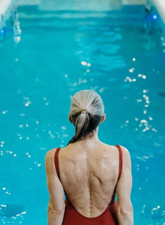 Person in a red swimsuit stands by a pool, viewed from behind.