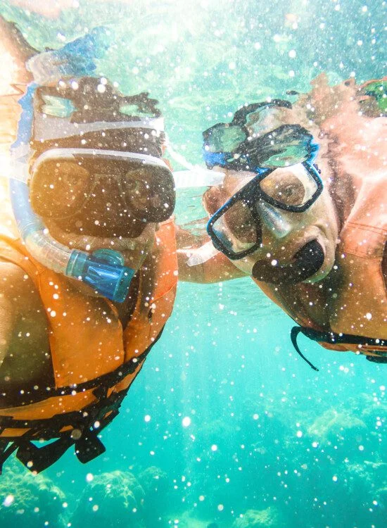 Two people snorkeling underwater, wearing orange vests and masks.