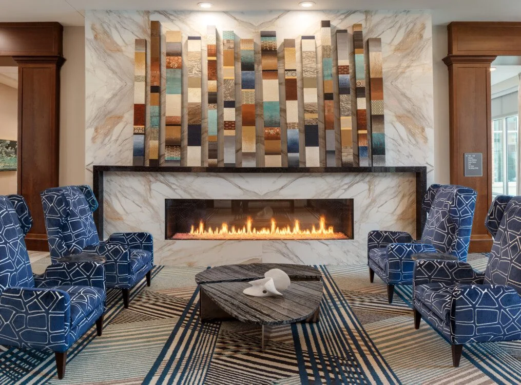 Elegant lounge with blue-patterned chairs, modern fireplace, abstract art, and a patterned rug.